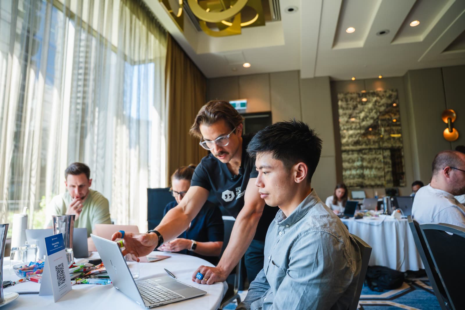 A coach leaning over to help a founder at his laptop during a workshop