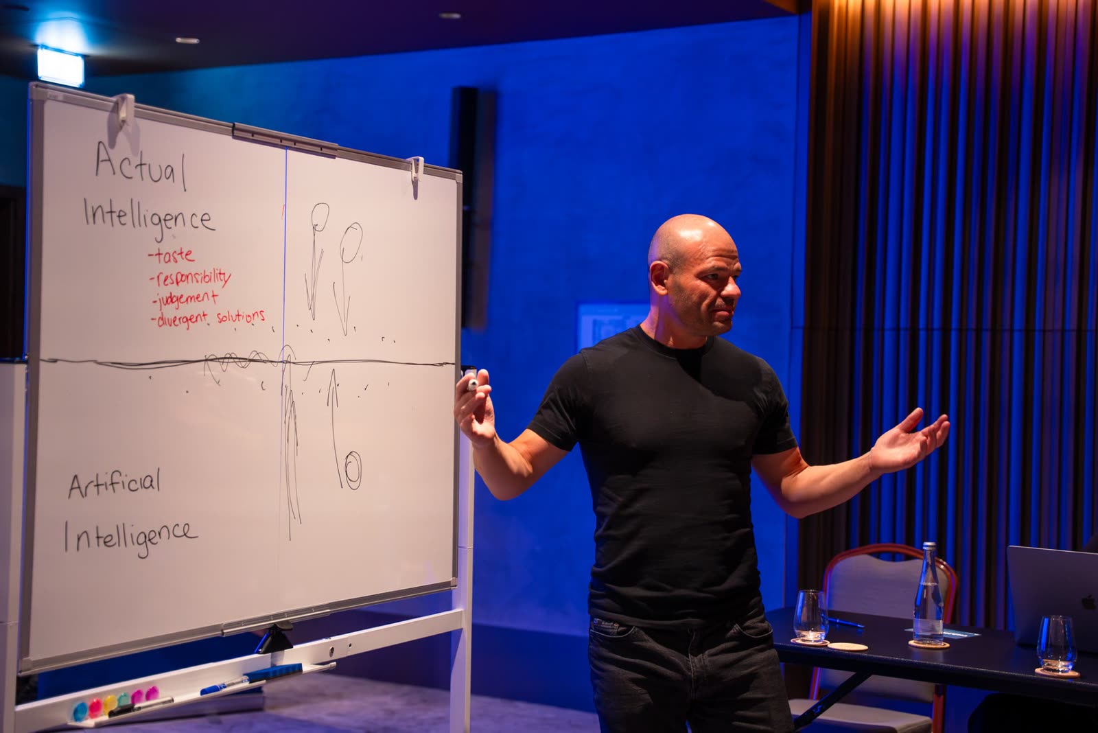 A speaker presenting at a whiteboard in a blue-lit room