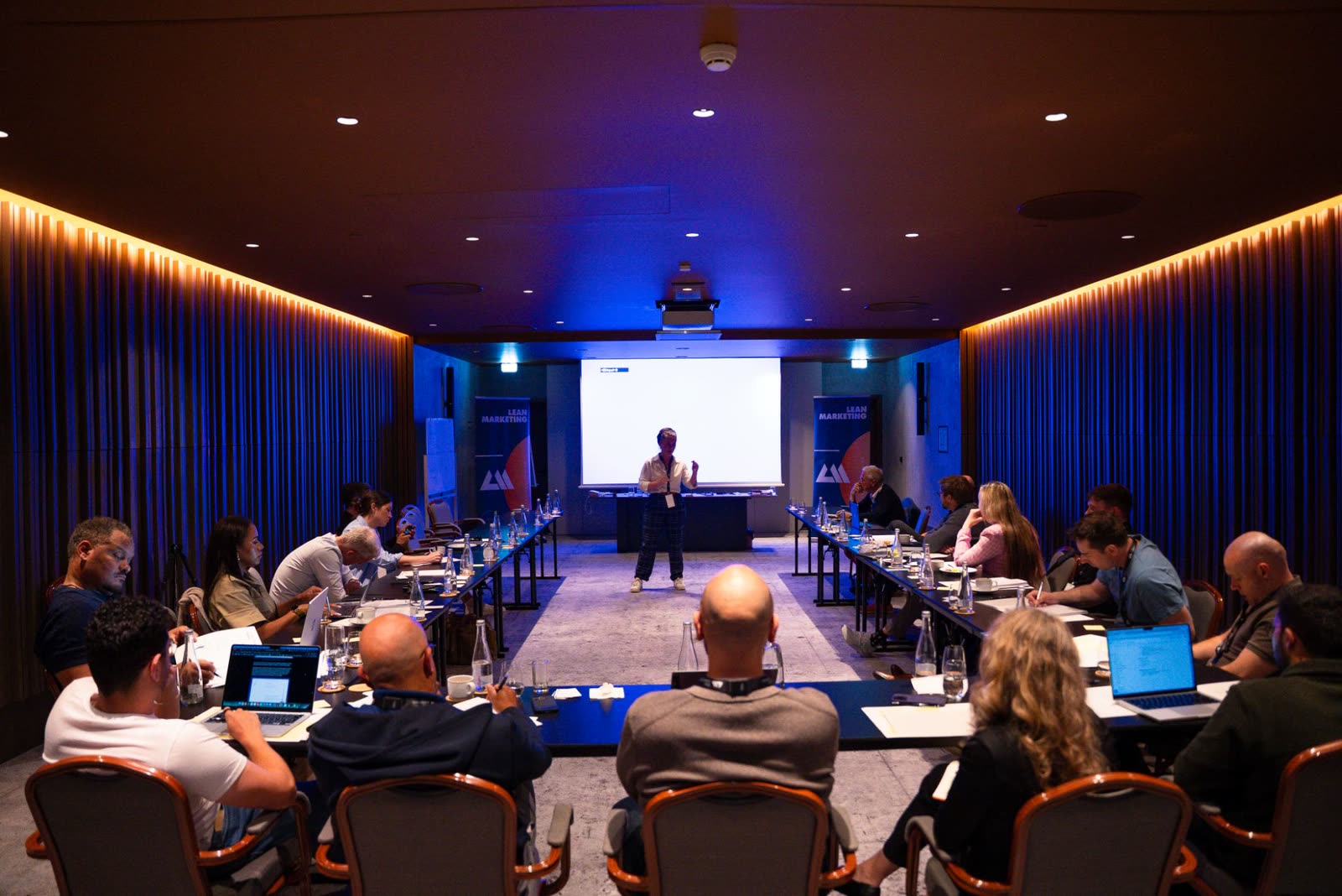 A workshop room of founders at long tables facing a speaker